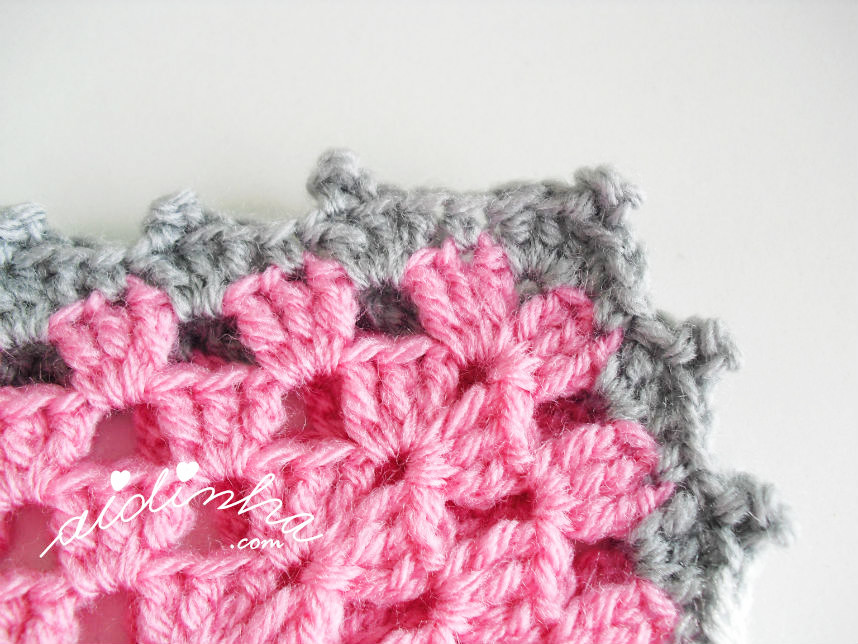 Foto do canto da volta de remate do poncho de crochet, rosa e cinza