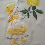 Pano de cozinha com boneca bordada, com aplicação de tecido e crochet